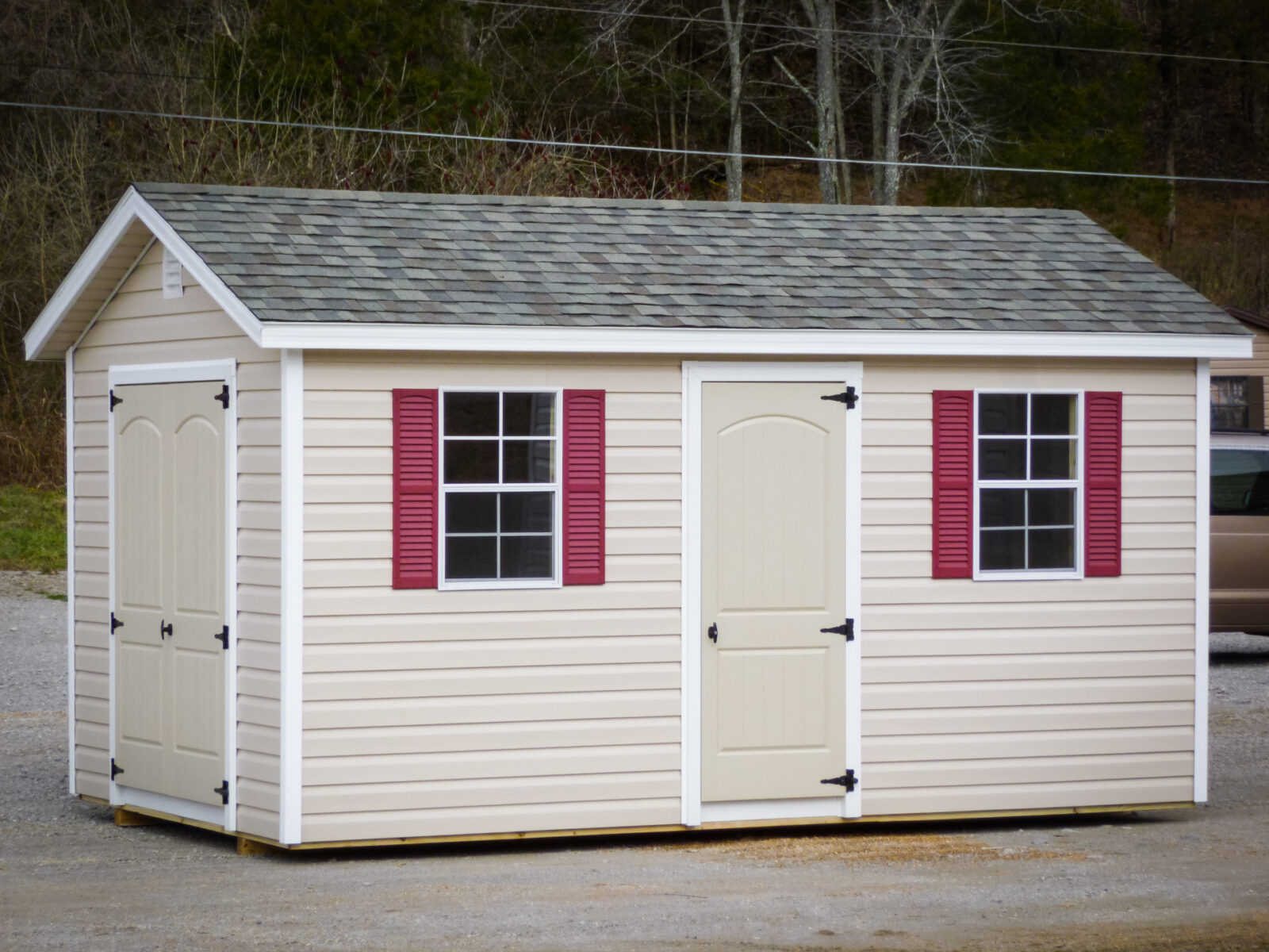 A storage shed in Kentucky with vinyl siding, double doors, and windows with red shutters
